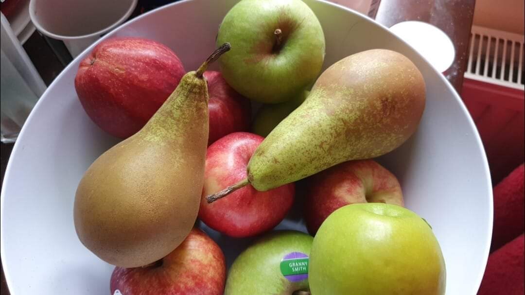 A photo of my fruit bowl. In it are five red royal gala apples, four green granny smith apples, and resting on top, my two remaining conference pears, green with brown bottoms.