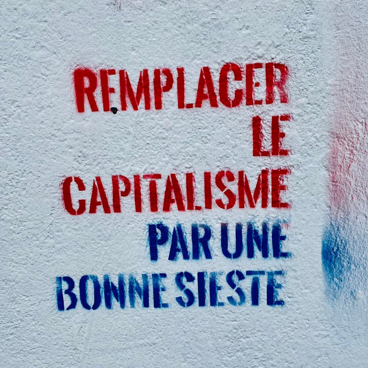 Red and blue stencil on a wall that says "Replace capitalism with a good nap" in French 