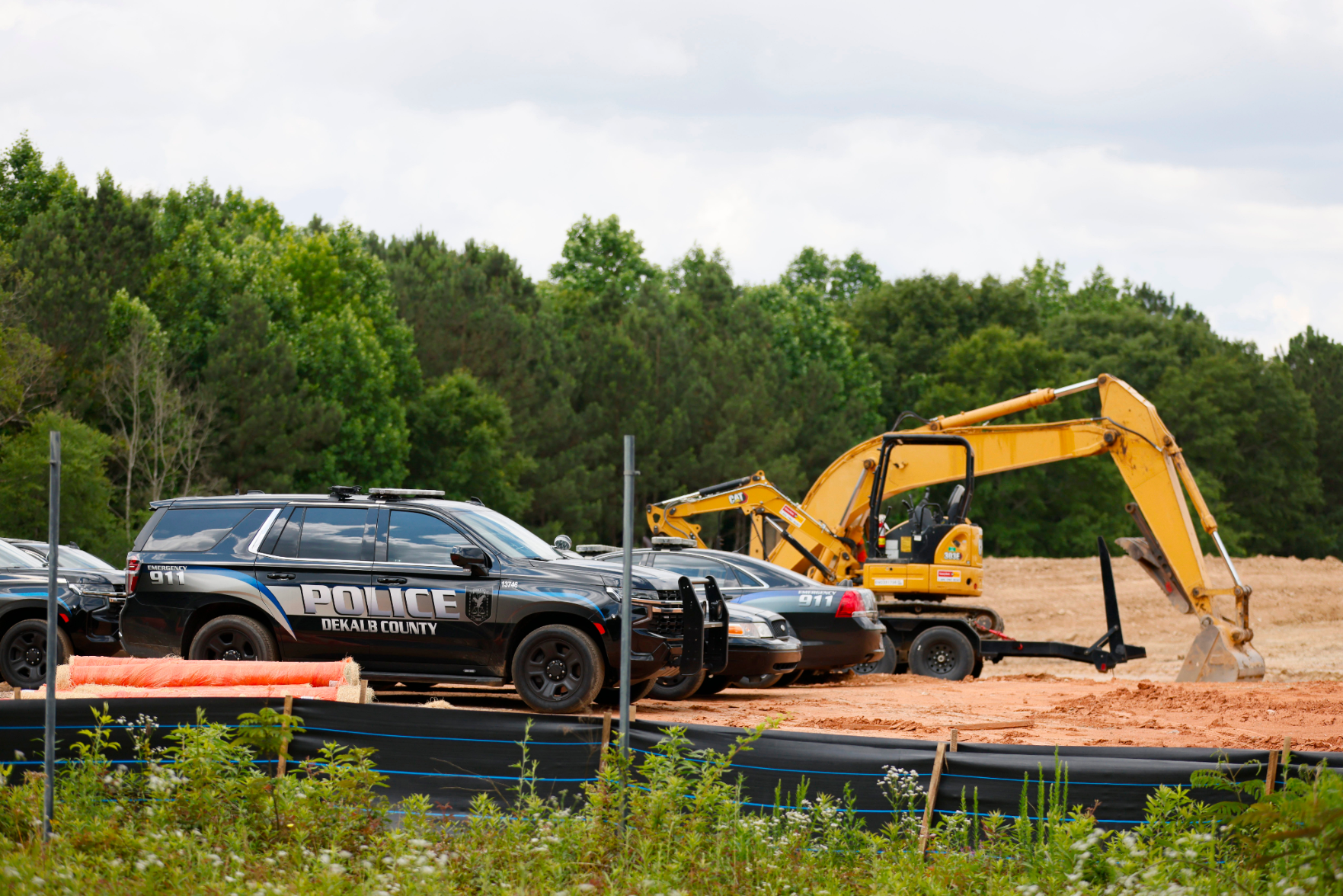 An image of police cars and construction equipment destroying the forest to build Cop City.