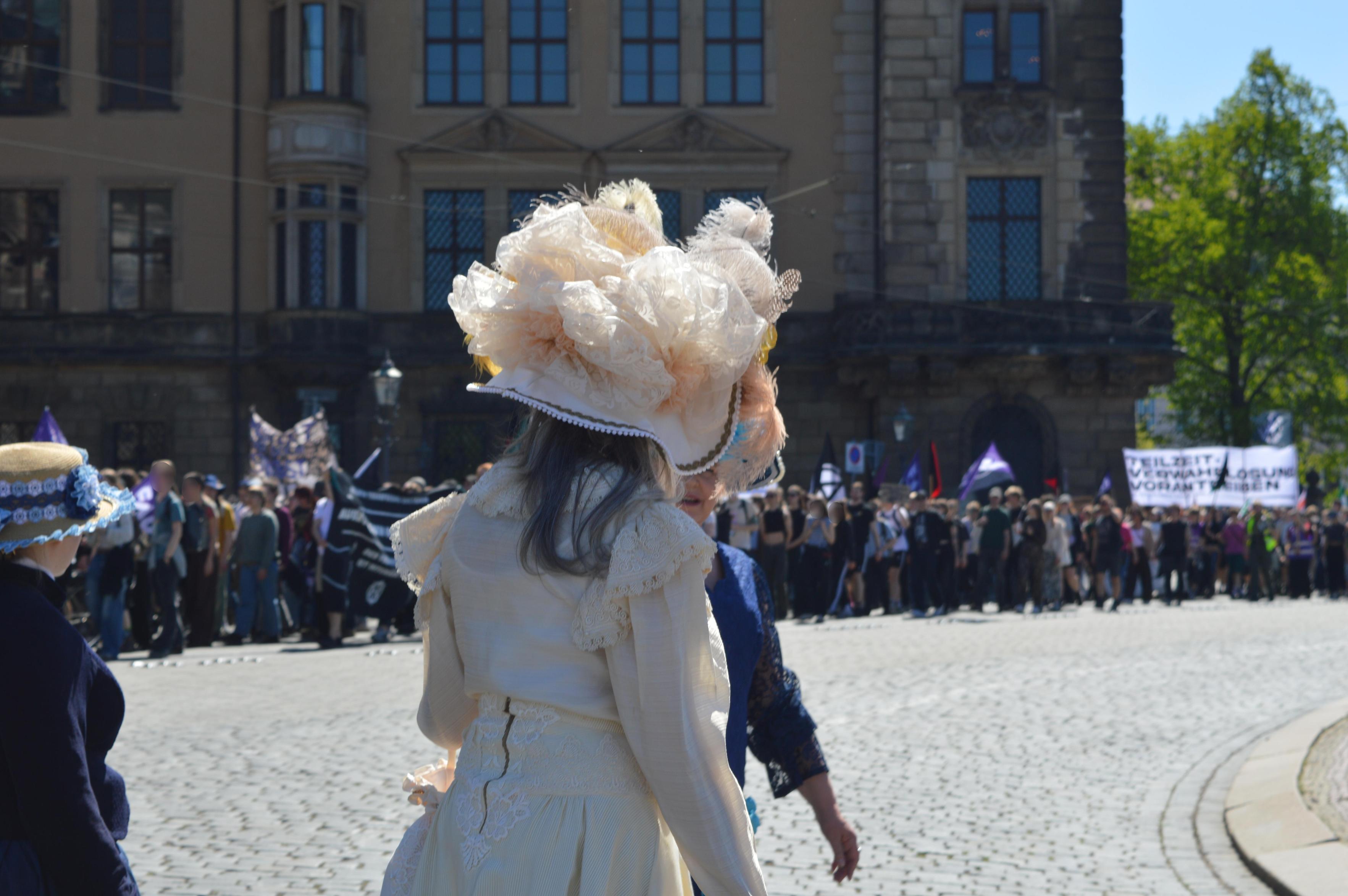 Leute in pompösen Barockkleidern blicken verwundert auf die anarchistische 1. Mai-Demo in Dresden