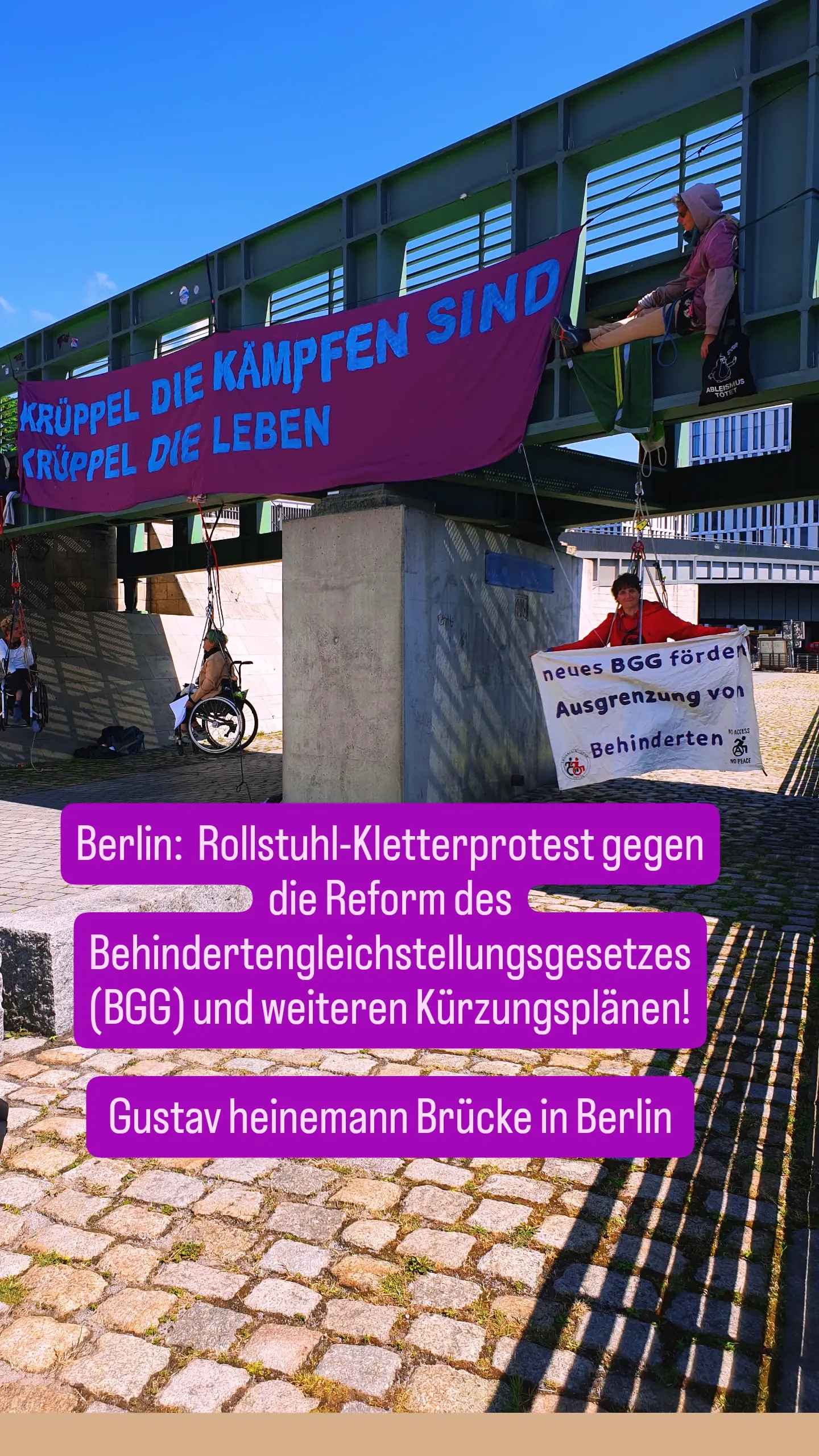 Banner an einer Brücke. " Krüppel die kämpfen sind Krüppel die leben" und 3 Menschen im Rollstuhl in Seilen gesichert